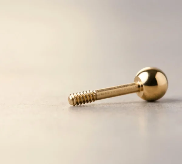 Gros plan sur un bijou de piercing en or massif présentant une finition miroir impeccable et une surface parfaitement lisse, symbolisant la sécurité et la biocompatibilité
