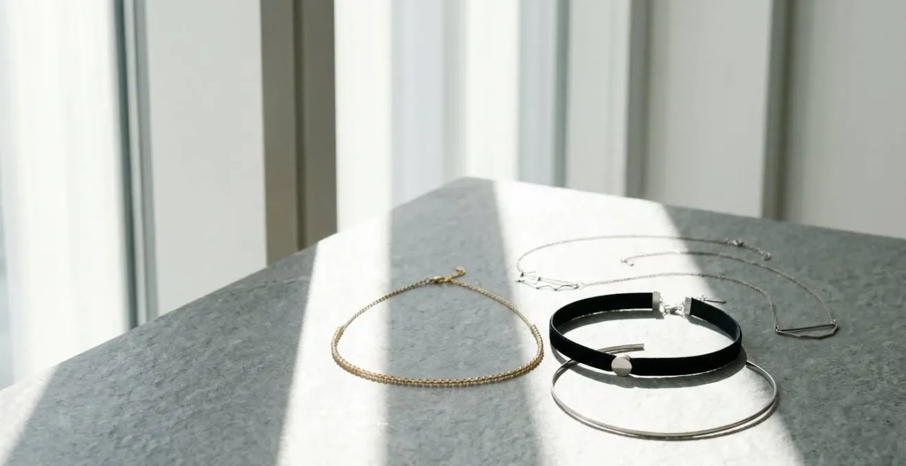 Composition minimaliste de chokers variés présentés sur une surface naturelle avec un jeu de verticales