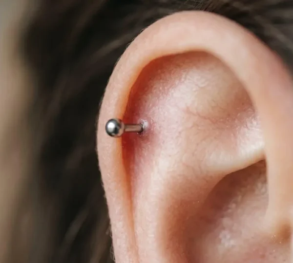 Gros plan artistique sur un cartilage d'oreille avec un piercing hélix en cours de cicatrisation, peau saine et bijou médical