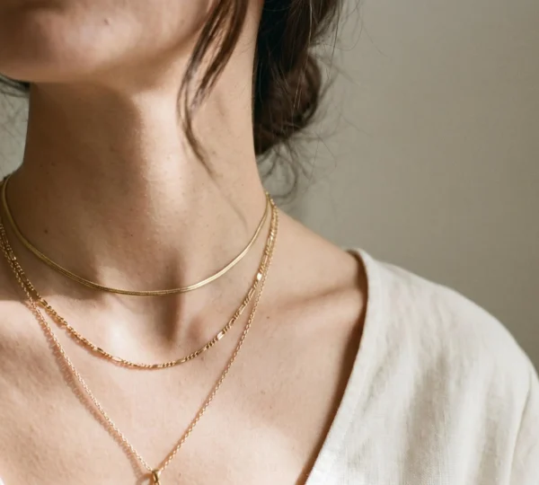 Décolleté féminin élégant portant trois colliers fins en or de longueurs différentes superposés harmonieusement